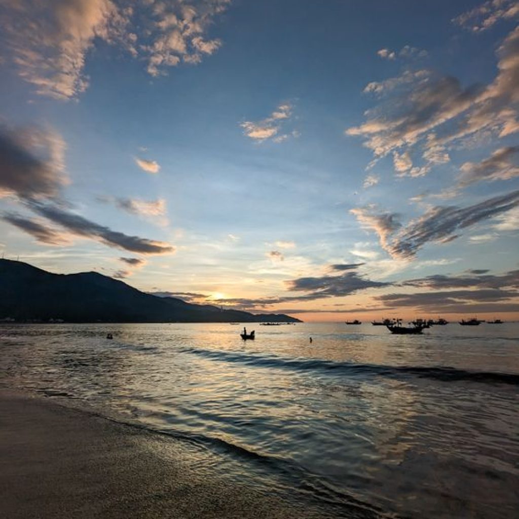 Sunrise over My Khe Beach in Da Nang, with traditional fishing boats silhouetted against a colorful sky