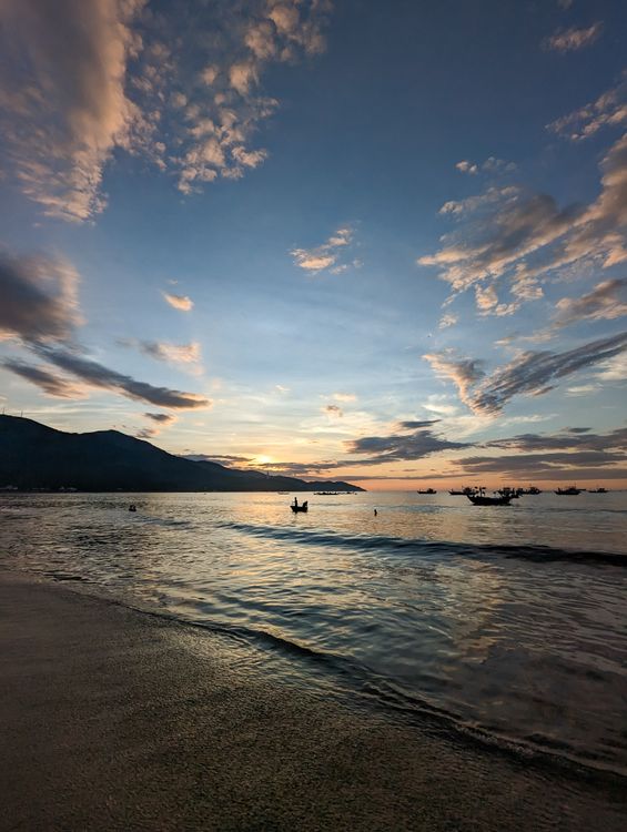 Sunrise over My Khe Beach in Da Nang, with traditional fishing boats silhouetted against a colorful sky