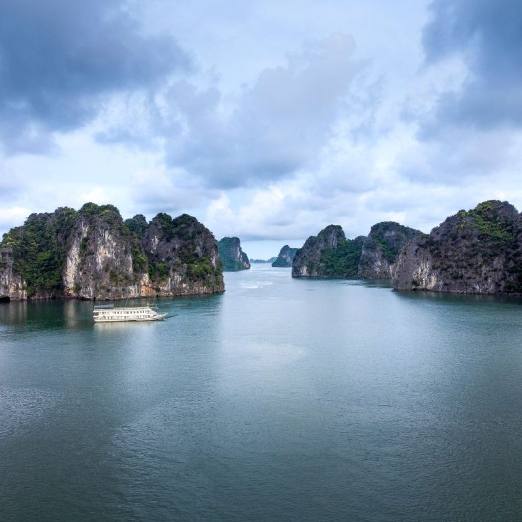 Aerial view of Halong Bay limestone karsts rising from emerald waters, with a cruise ship navigating between the islands