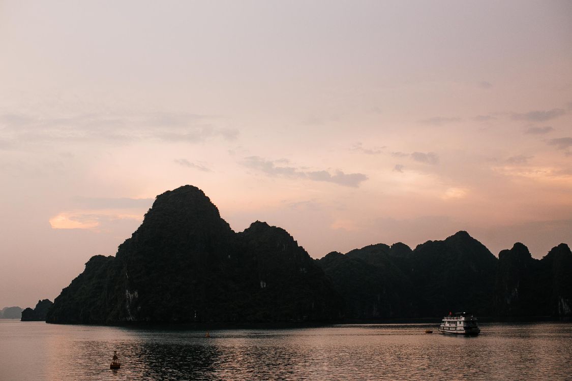 Peaceful sunset over Halong Bay with a traditional boat silhouetted against the orange sky and limestone cliffs