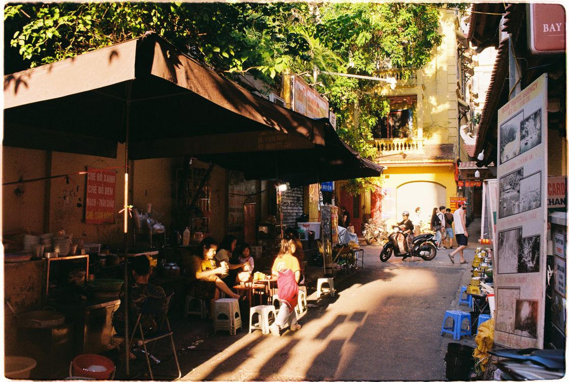 Sunlit street food alley in Hanoi with vendors and outdoor seating