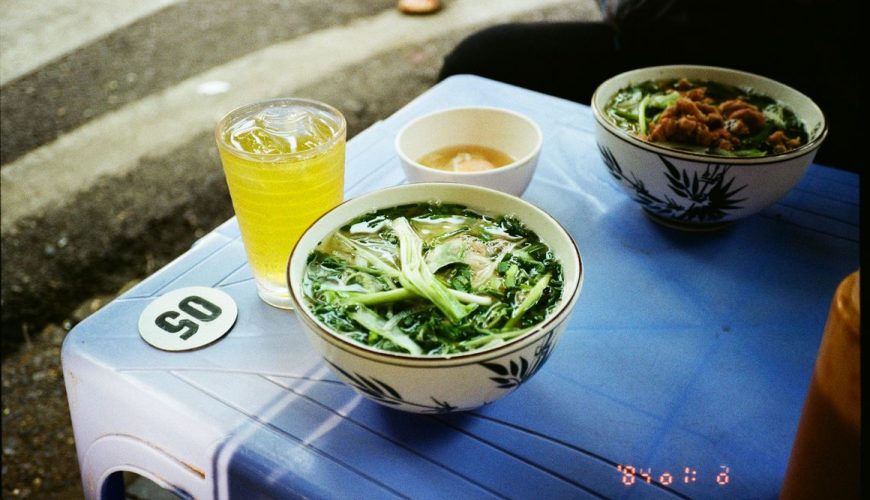 Street food scene in Hanoi with a steaming bowl of pho served on a plastic stool