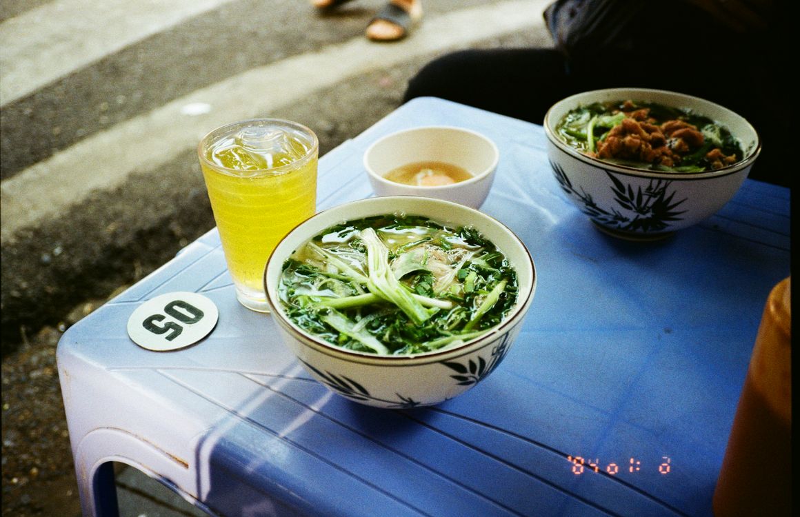 Street food scene in Hanoi with a steaming bowl of pho served on a plastic stool