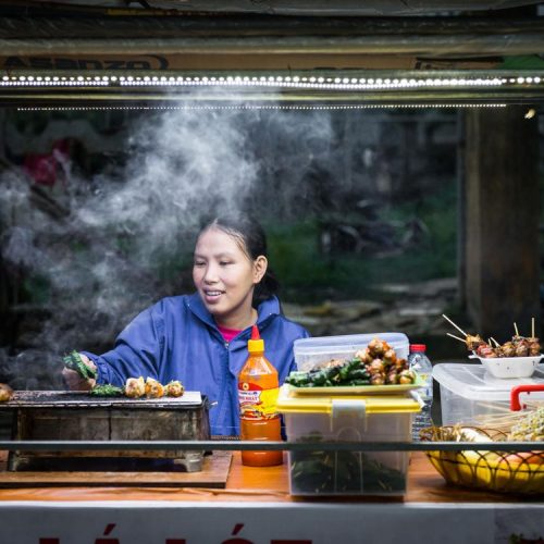 Woman cooking street food at Hoi An night market in Vietnam - traditional grilled skewers