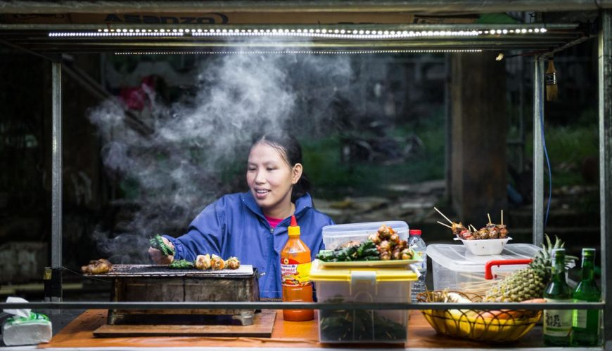 Woman cooking street food at Hoi An night market in Vietnam - traditional grilled skewers