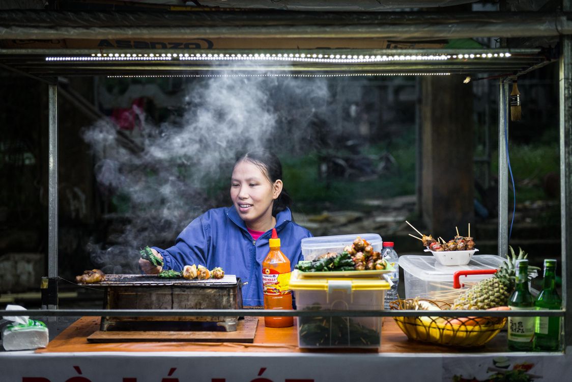 Woman cooking street food at Hoi An night market in Vietnam - traditional grilled skewers
