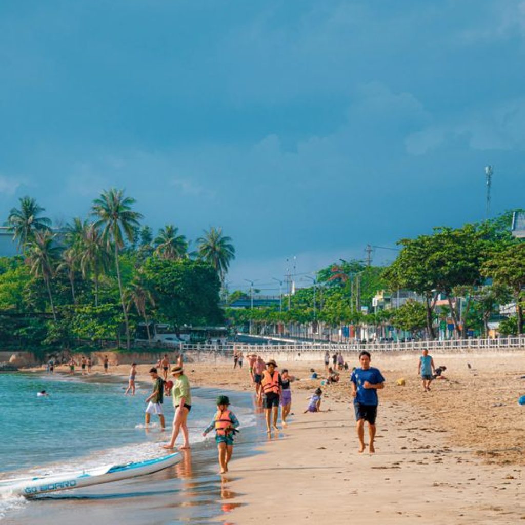 Sunny day at Nha Trang beach with clear blue water and people enjoying the coast