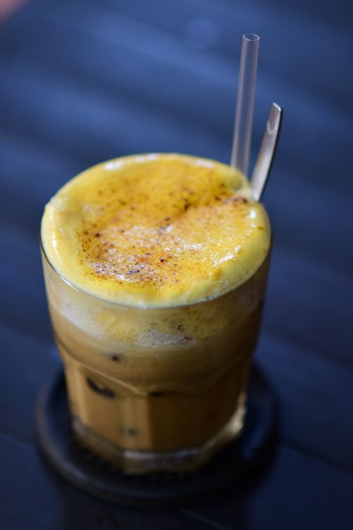 A glass of Vietnamese egg coffee with thick golden foam topping served on a dark table