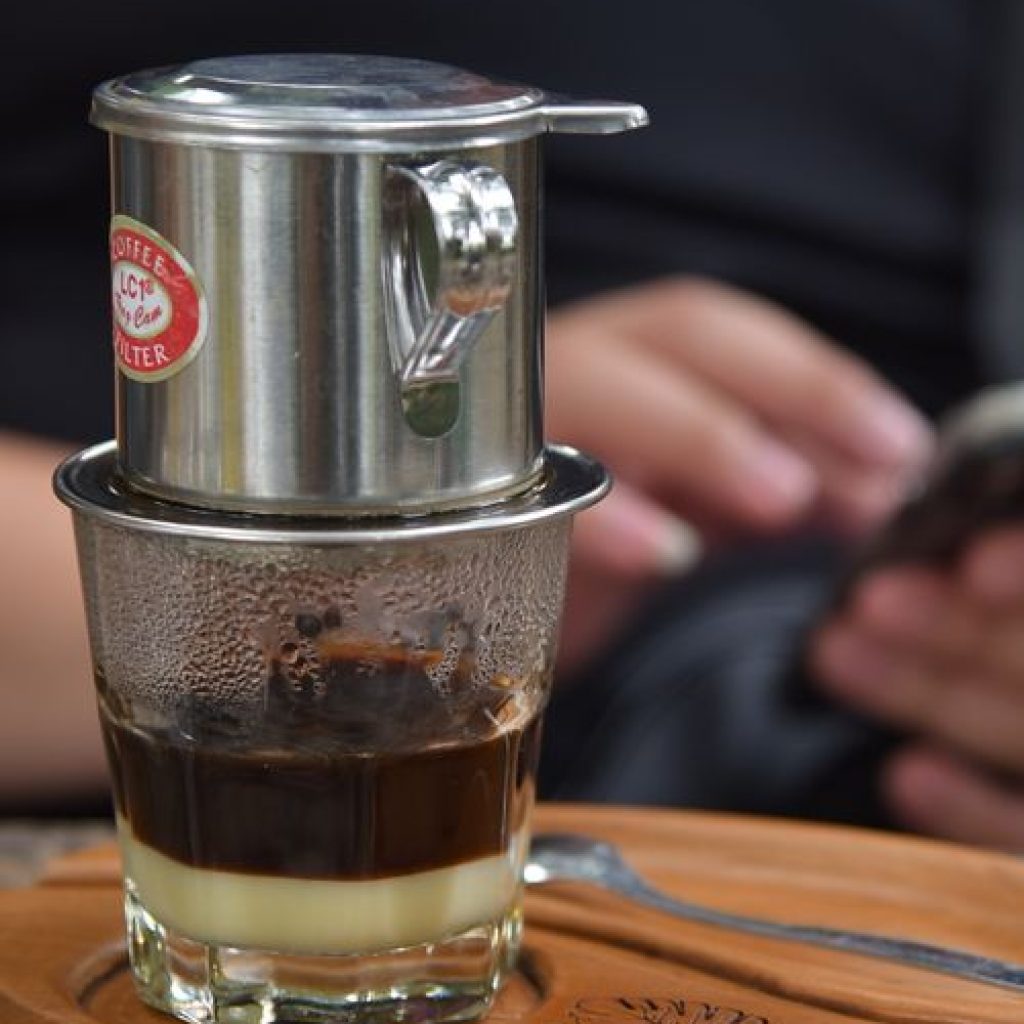 Vietnamese coffee dripping through a traditional phin filter over a glass of condensed milk