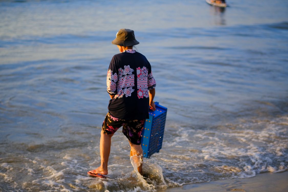 Local fisherman walking on My Khe Beach in Da Nang at sunrise with traditional boats