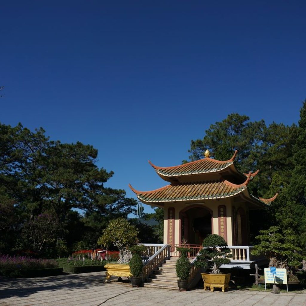 Scenic view of a traditional pagoda in Da Lat, Vietnam — surrounded by lush greenery under a clear blue sky.