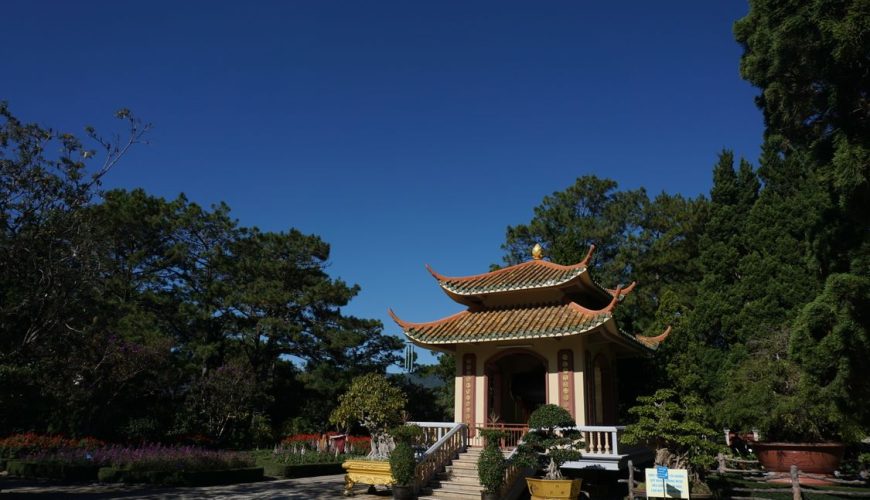 Scenic view of a traditional pagoda in Da Lat, Vietnam — surrounded by lush greenery under a clear blue sky.