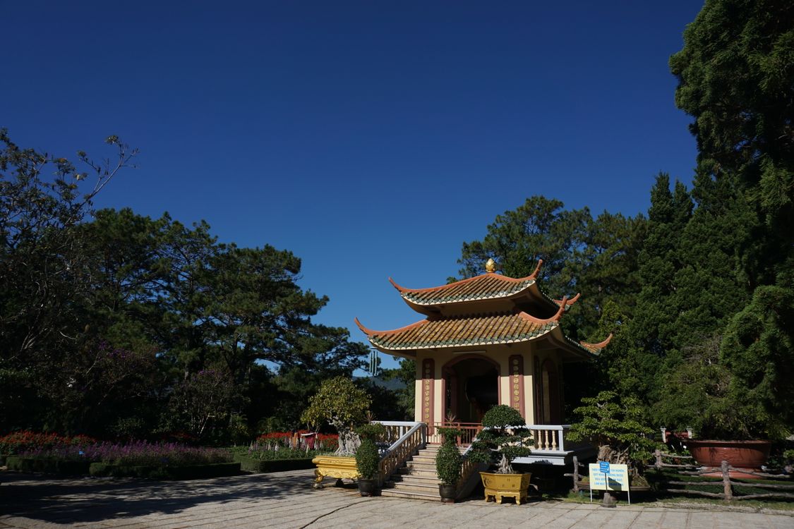 Scenic view of a traditional pagoda in Da Lat, Vietnam — surrounded by lush greenery under a clear blue sky.
