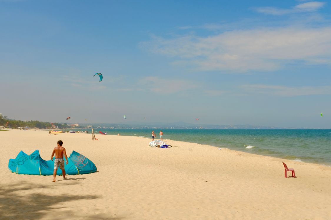 Kite surfers on Mui Ne beach with colorful kites against blue sky