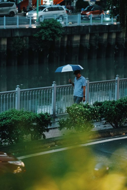 A man walking with an umbrella by a canal in Vietnam during the rainy season — July brings afternoon showers across much of the country