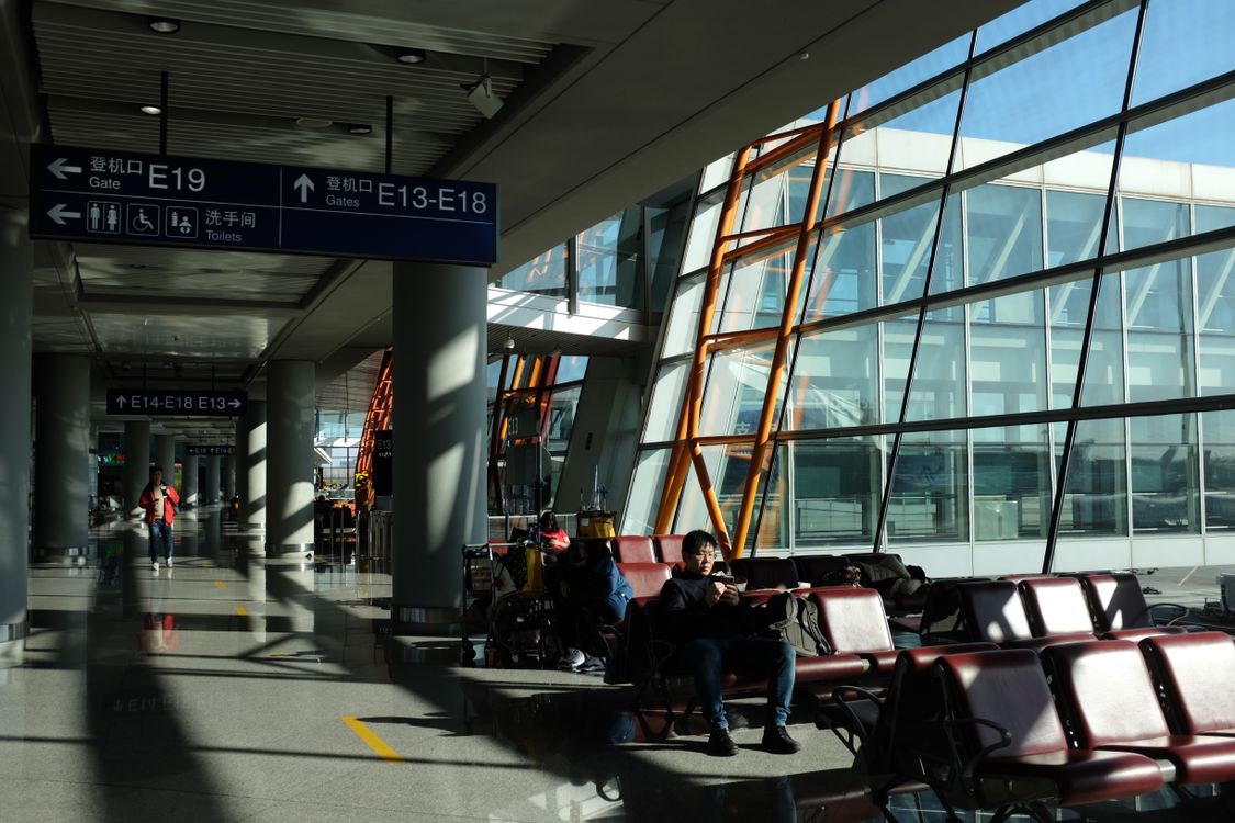 Travelers waiting inside a busy airport terminal with directional signs