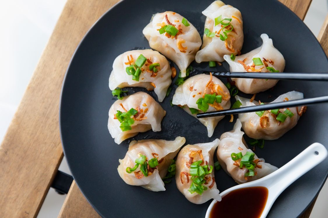 Close-up of steamed dumplings on a plate with soy sauce and fresh greens