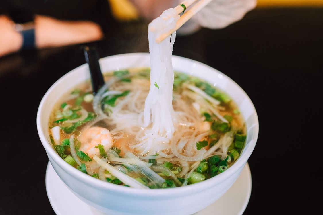 A steaming bowl of Vietnamese noodle soup with fresh herbs and chopsticks