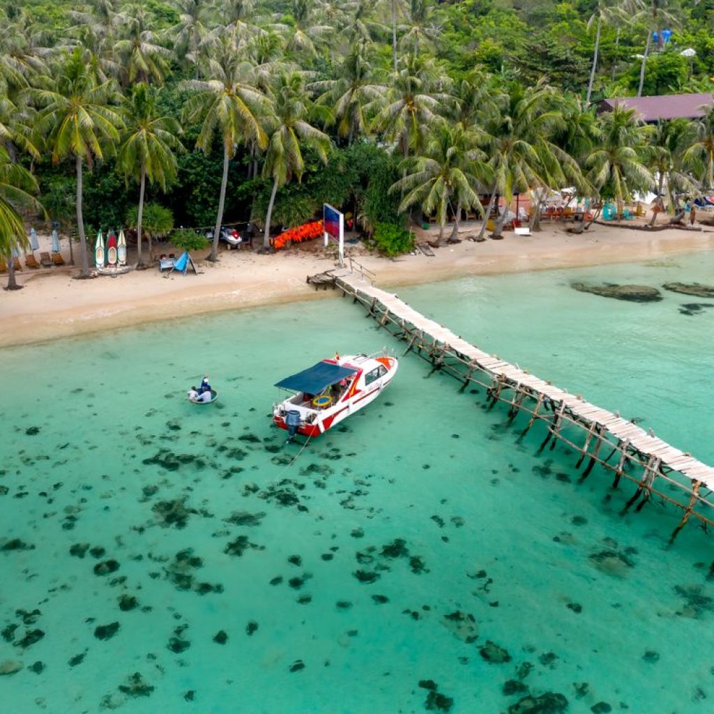 Aerial view of a tropical beach with a pier and speedboat, the kind of crossing you take from Hoi An to Cham Island
