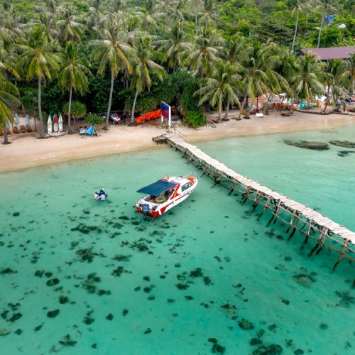 Aerial view of a tropical beach with a pier and speedboat, the kind of crossing you take from Hoi An to Cham Island