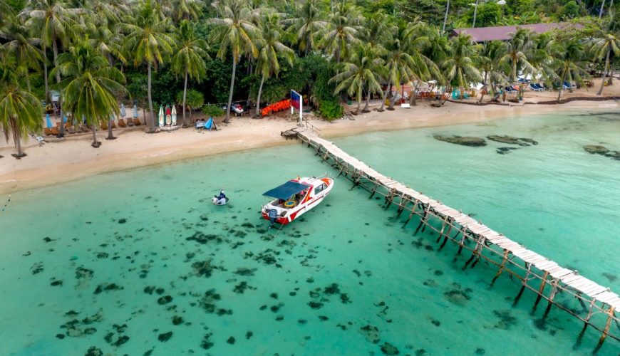 Aerial view of a tropical beach with a pier and speedboat, the kind of crossing you take from Hoi An to Cham Island