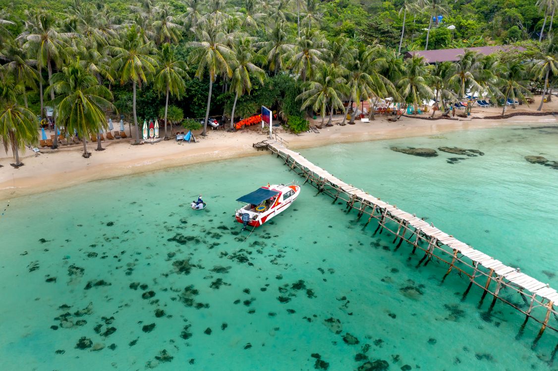 Aerial view of a tropical beach with a pier and speedboat, the kind of crossing you take from Hoi An to Cham Island