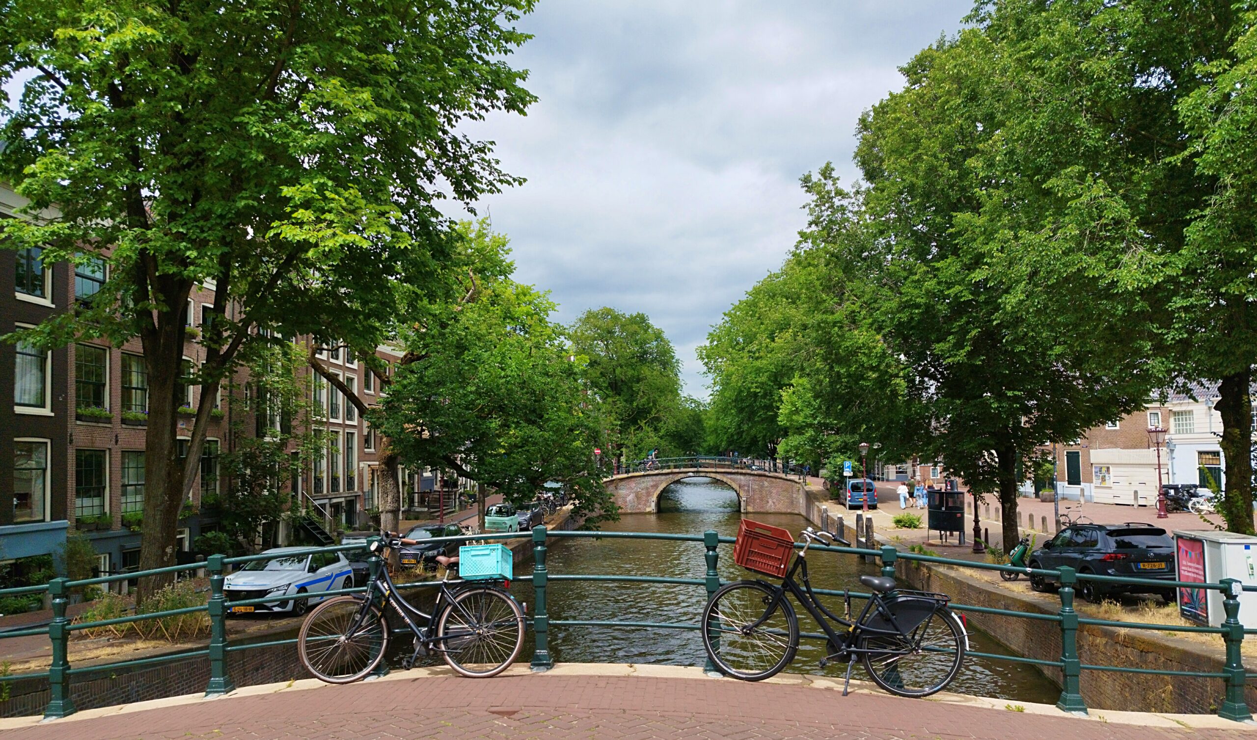 Bicycles parked beside a canal bridge beneath leafy trees in Amsterdam.