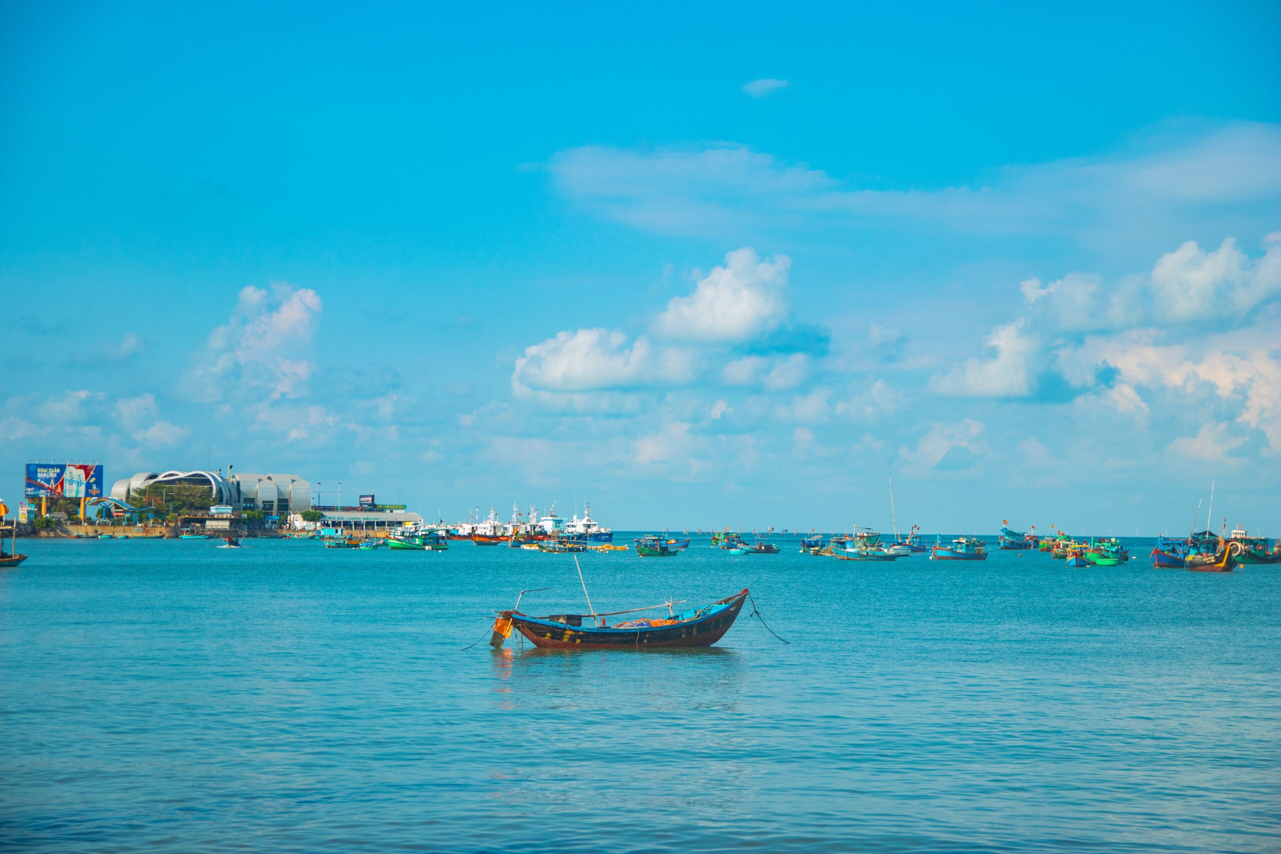 Colourful wooden fishing boats moored along a Vietnamese harbour quay with waterfront buildings behind
