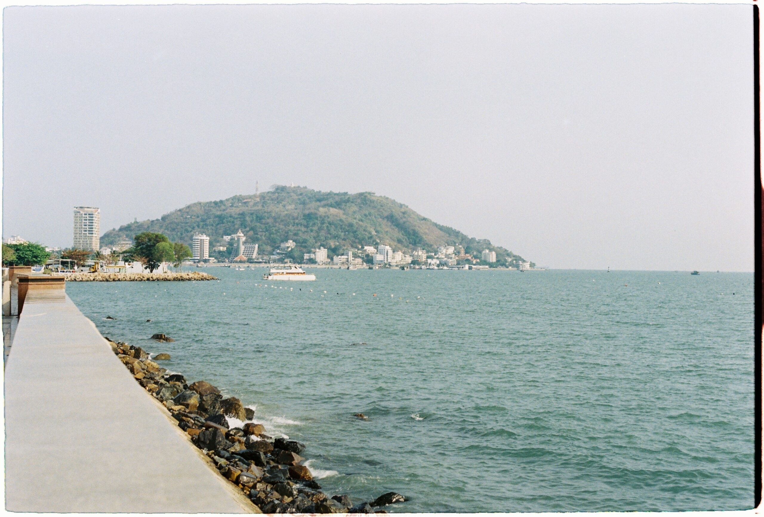 Seafront promenade and sheltered bay with passenger boats and waterfront buildings below wooded hills