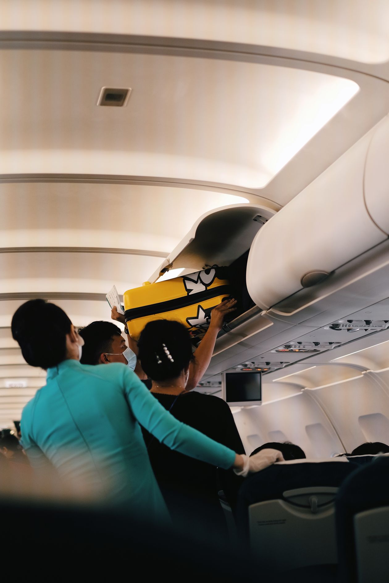 Passengers lifting a yellow suitcase into an airplane overhead bin