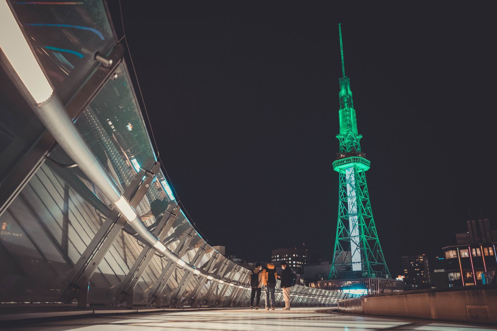 Green-lit MIRAI TOWER beside a curved elevated walkway in Nagoya