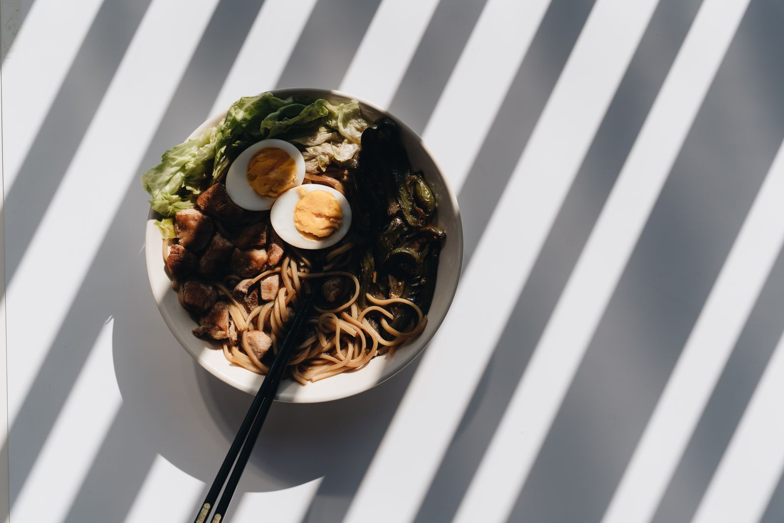Noodle bowl with halved eggs and greens on a sunlit table