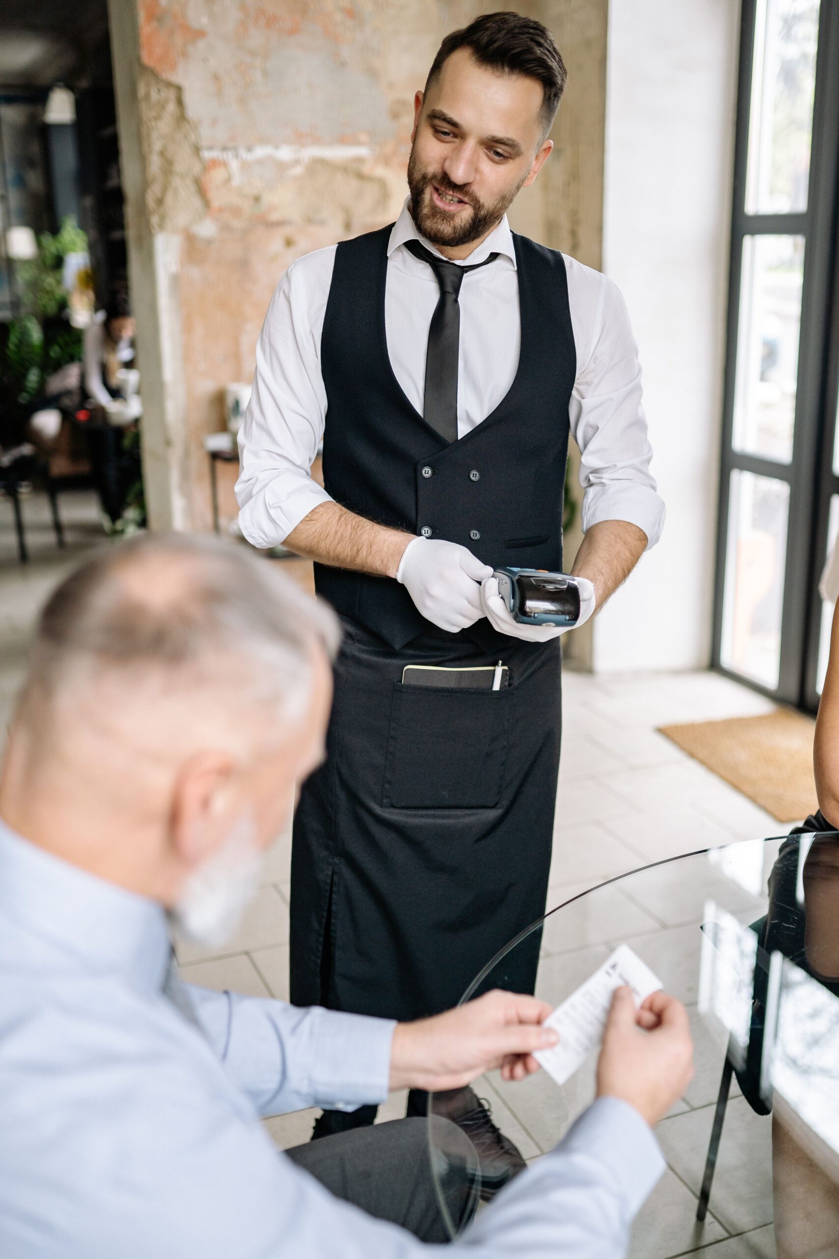 A customer reviews a receipt while a waiter holds a payment terminal