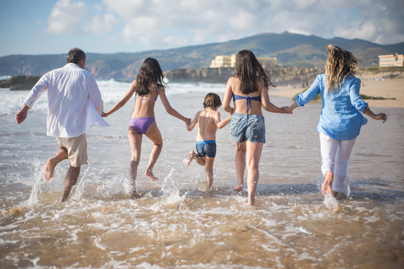 Family running hand in hand into shallow ocean waves on a sunny beach