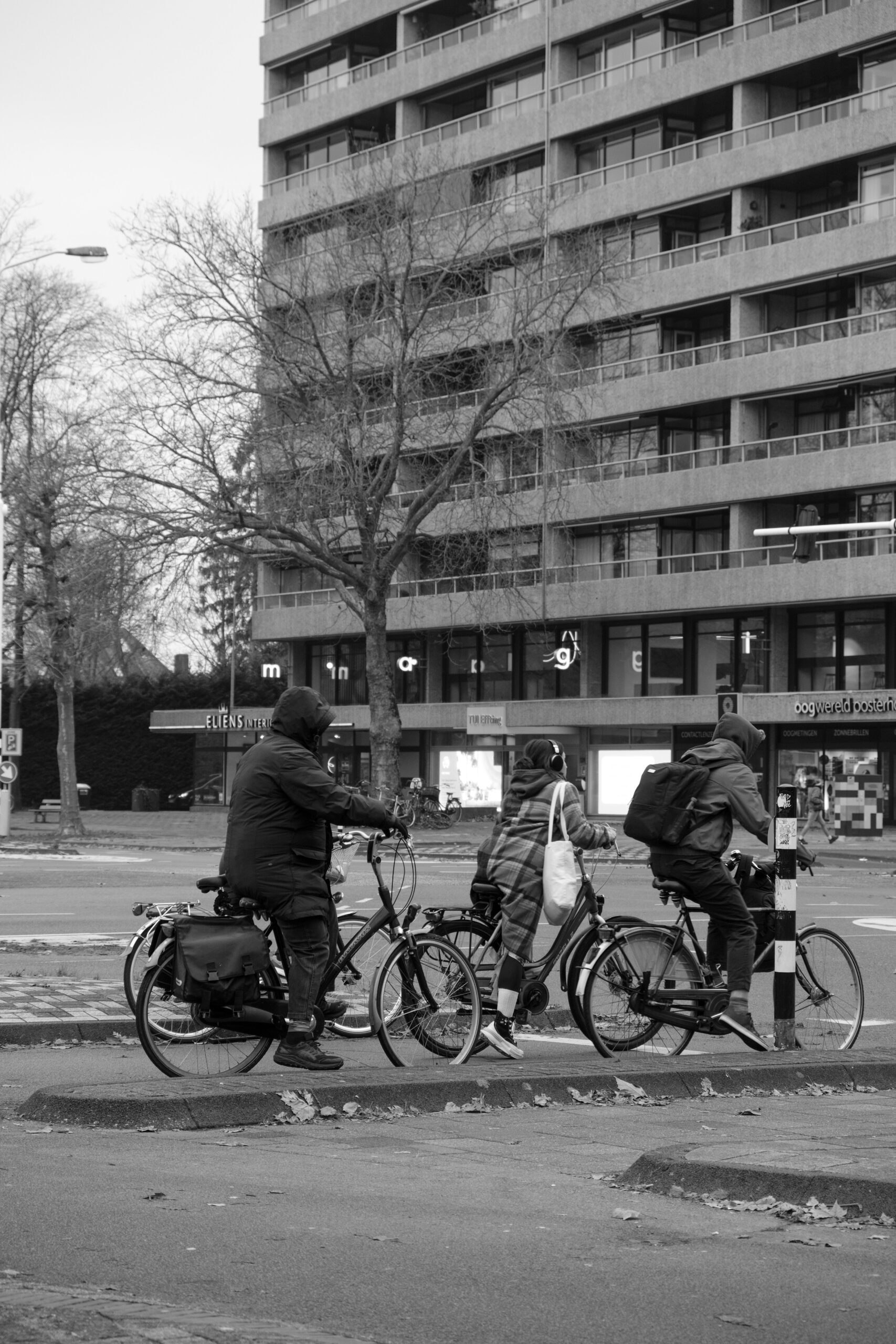 Cyclists ride across an Eindhoven street in front of a multi-storey urban building.