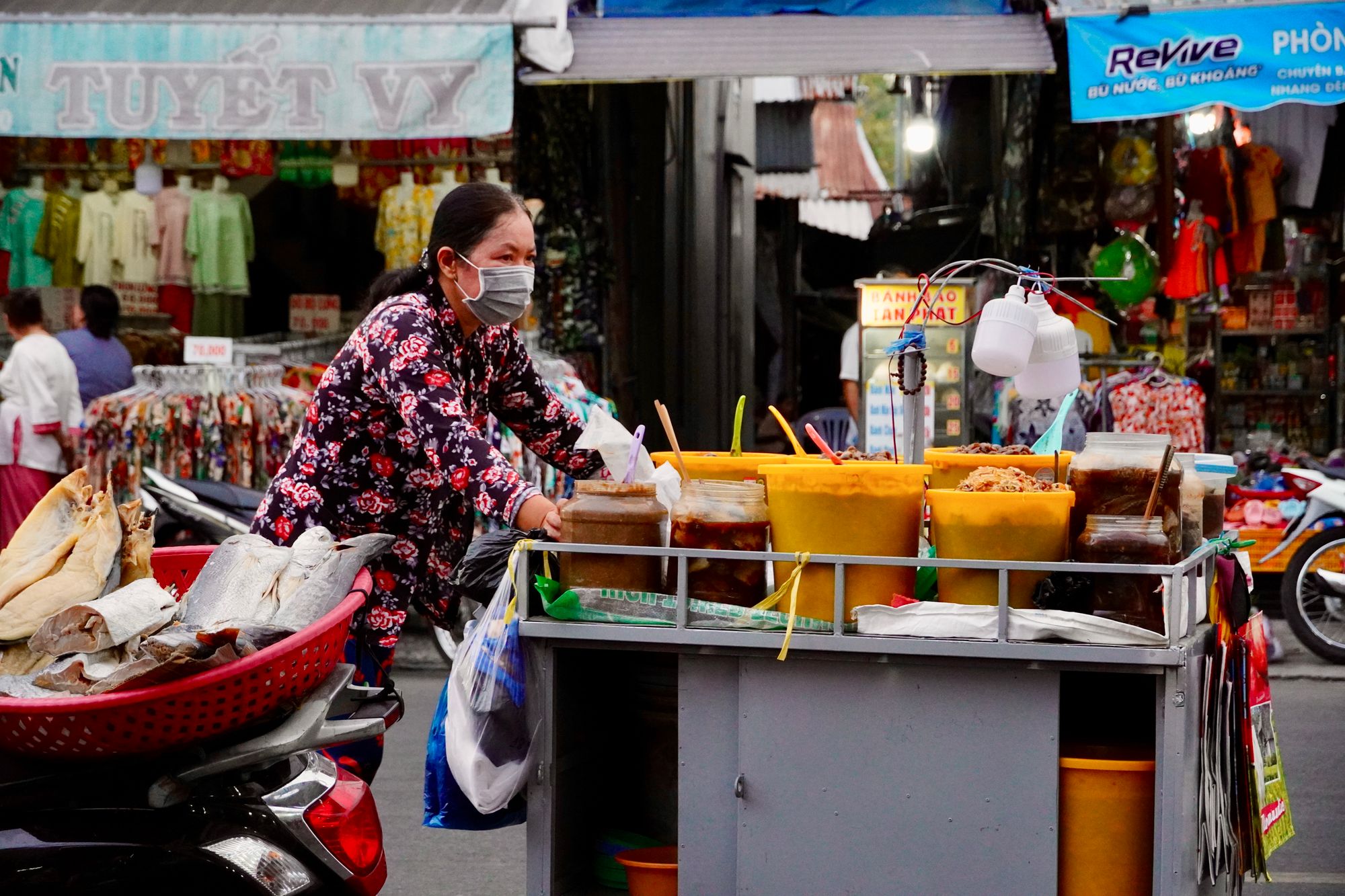 Street-food vendor serving ingredients from a cart in a busy market.