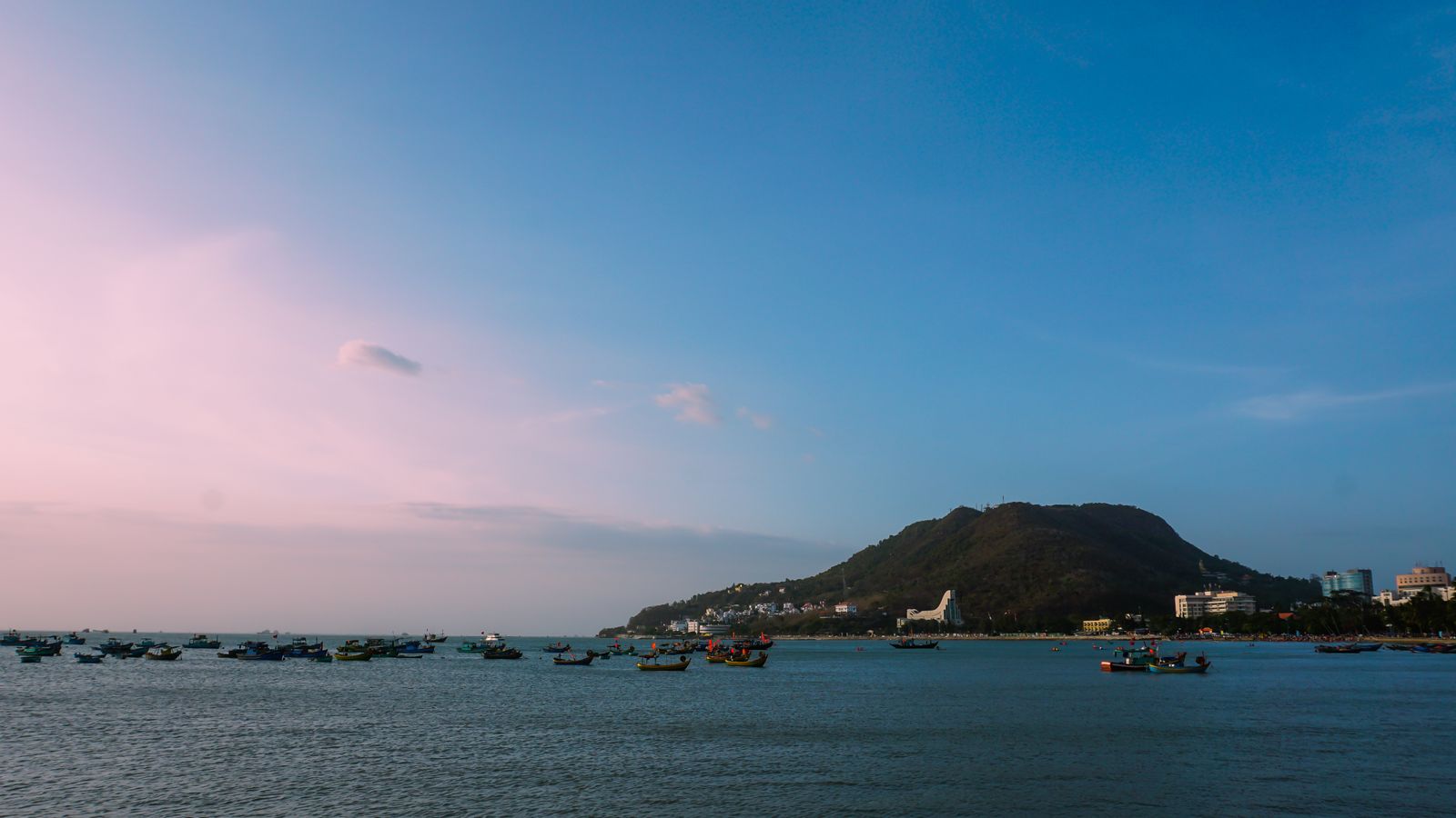 Fishing boats on a coastal bay with green hills and buildings in Vung Tau