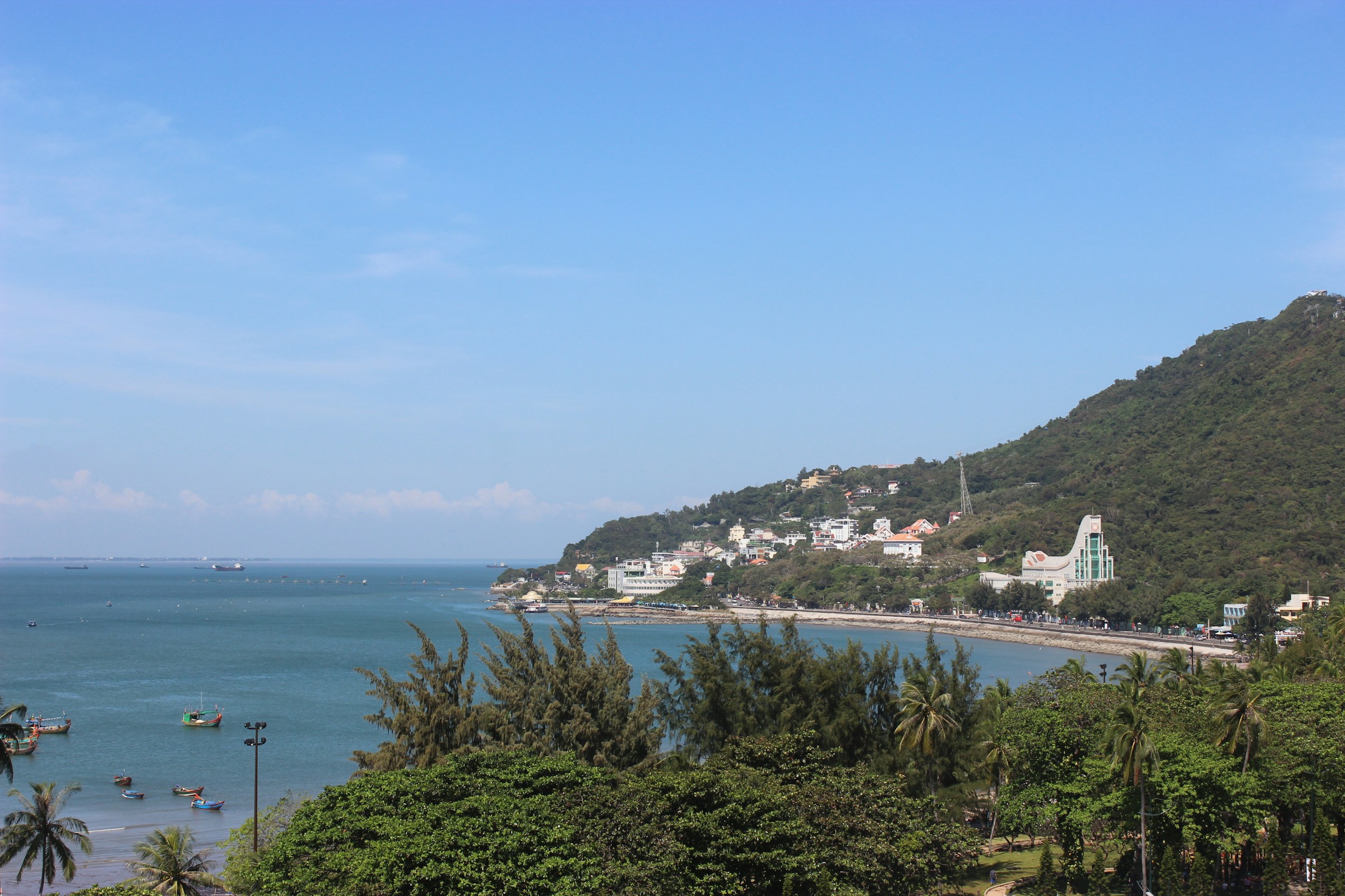 Fishing boats on calm water beside the green hillside waterfront of Vung Tau, Vietnam