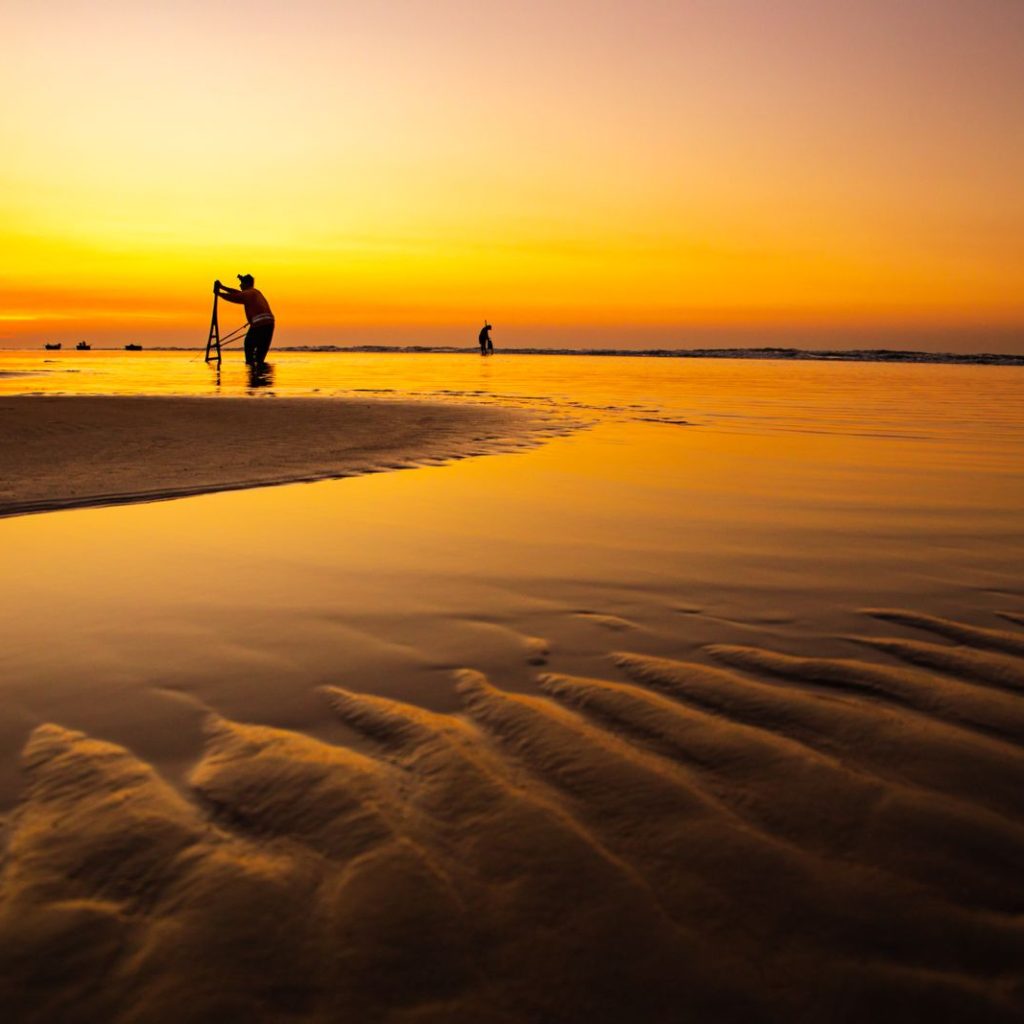 Golden sunset reflected on wet sand at Ho Tram Beach with silhouetted people