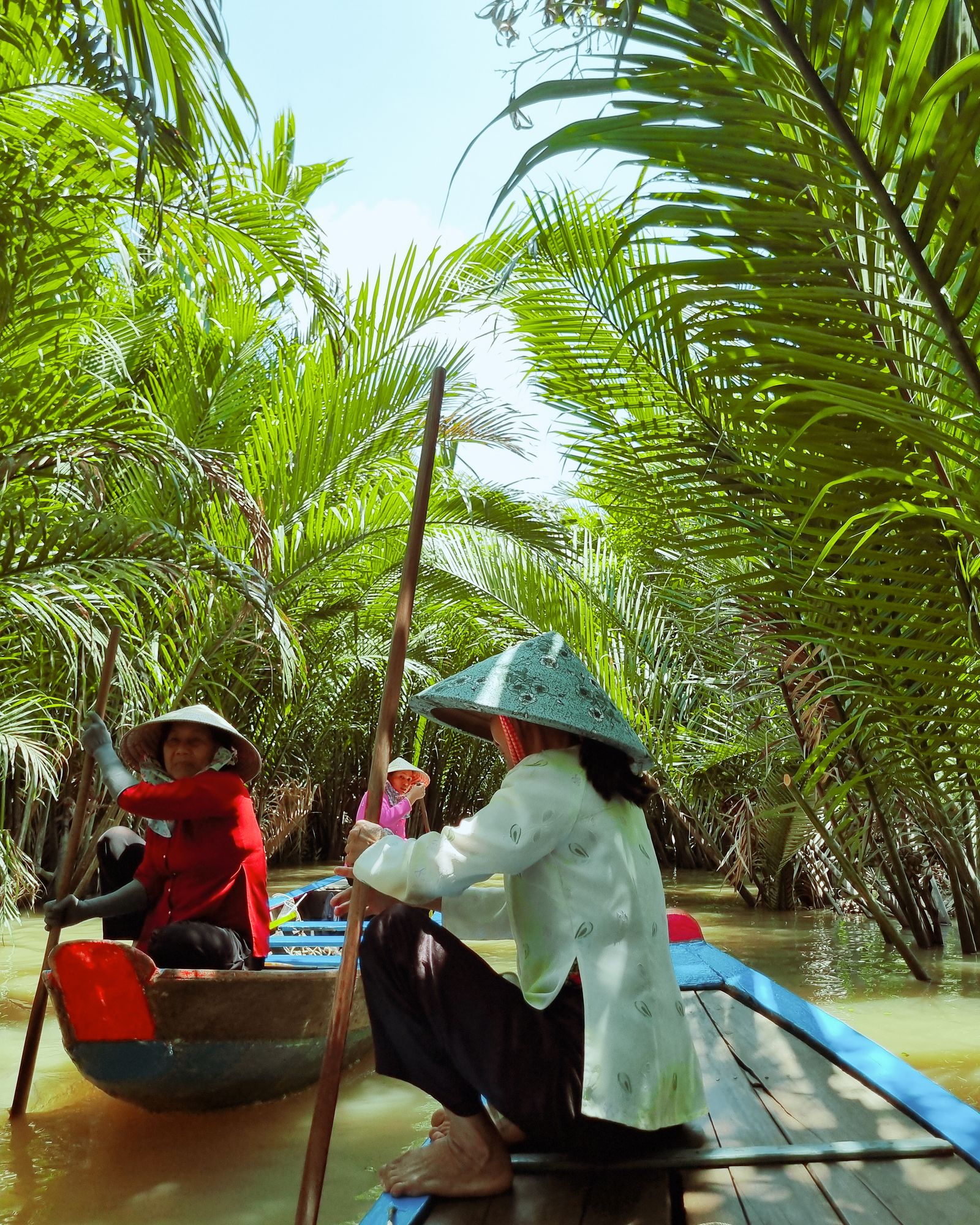 Local rowers guiding wooden boats through a palm-lined Mekong Delta canal