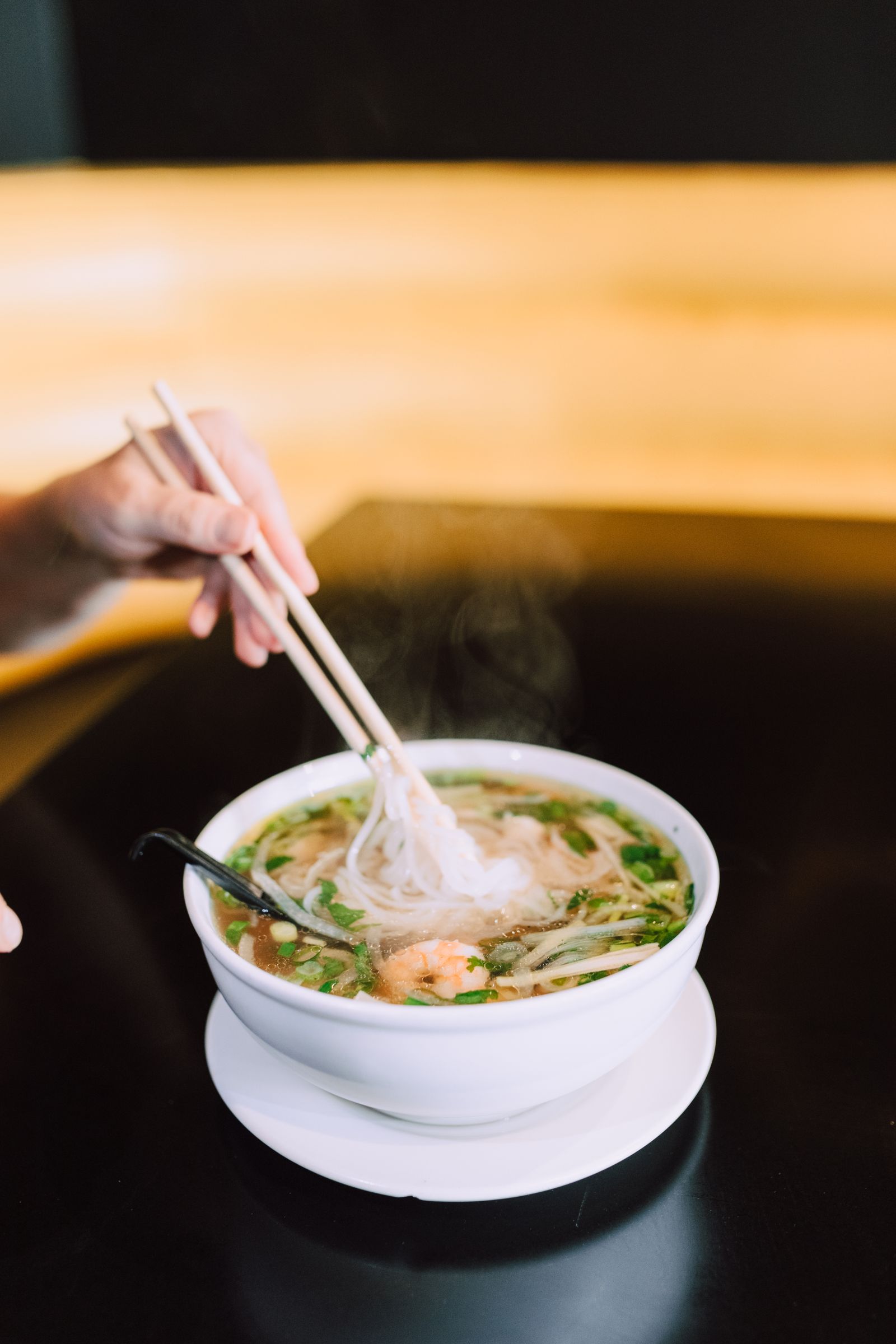 Steaming bowl of Vietnamese pho with herbs and chopsticks