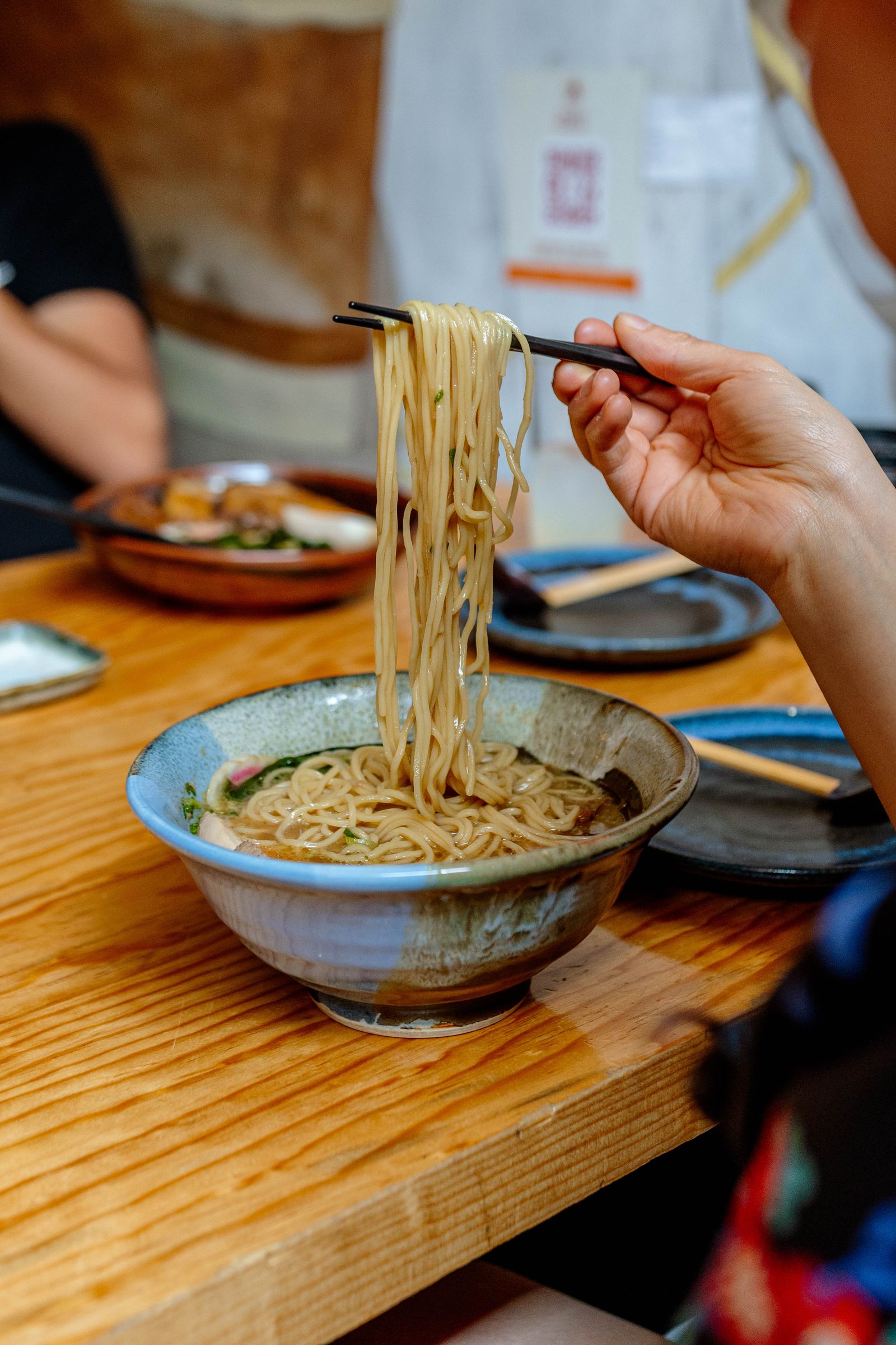 Chopsticks lifting noodles above a soup bowl