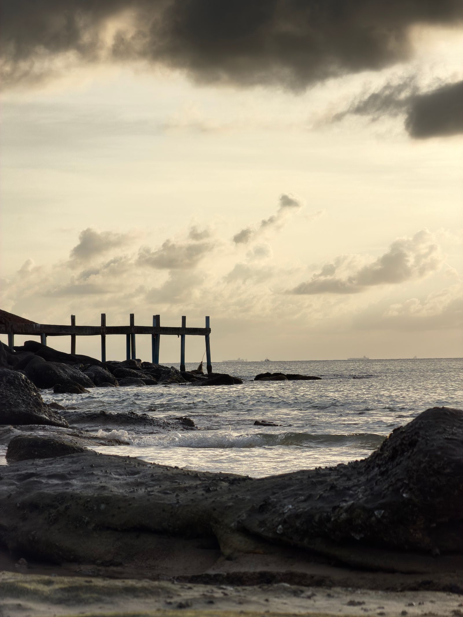 Rocky Phu Quoc shoreline with a wooden pier and layered tropical clouds over the Gulf of Thailand at golden hour