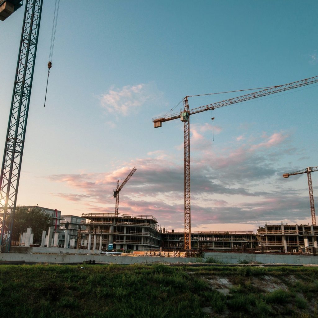 Tower cranes above a large unfinished building complex at sunset