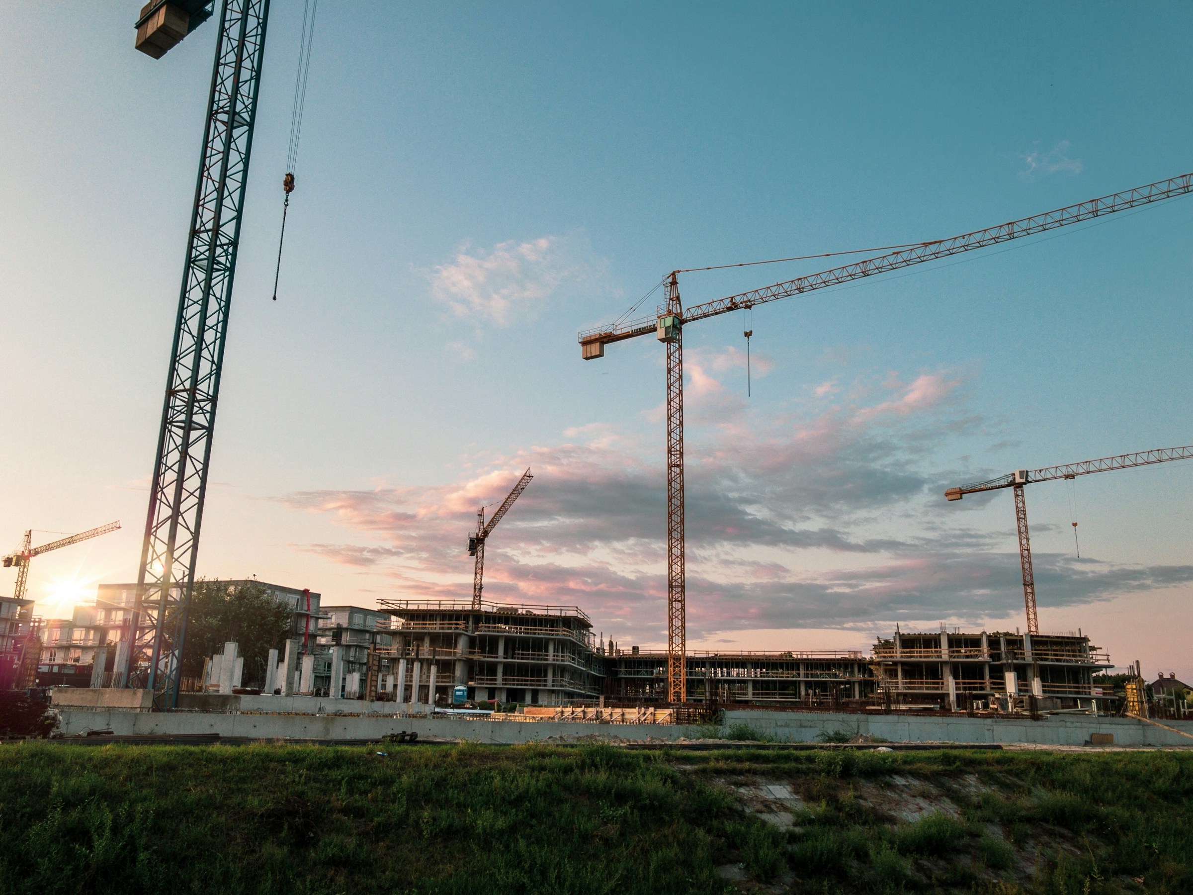 Tower cranes above a large unfinished building complex at sunset