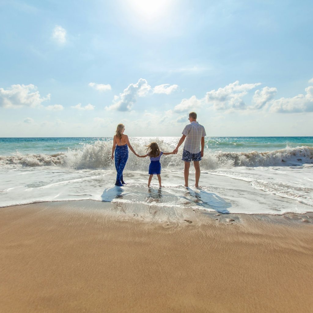 Two adults and a child holding hands together at the edge of the sea