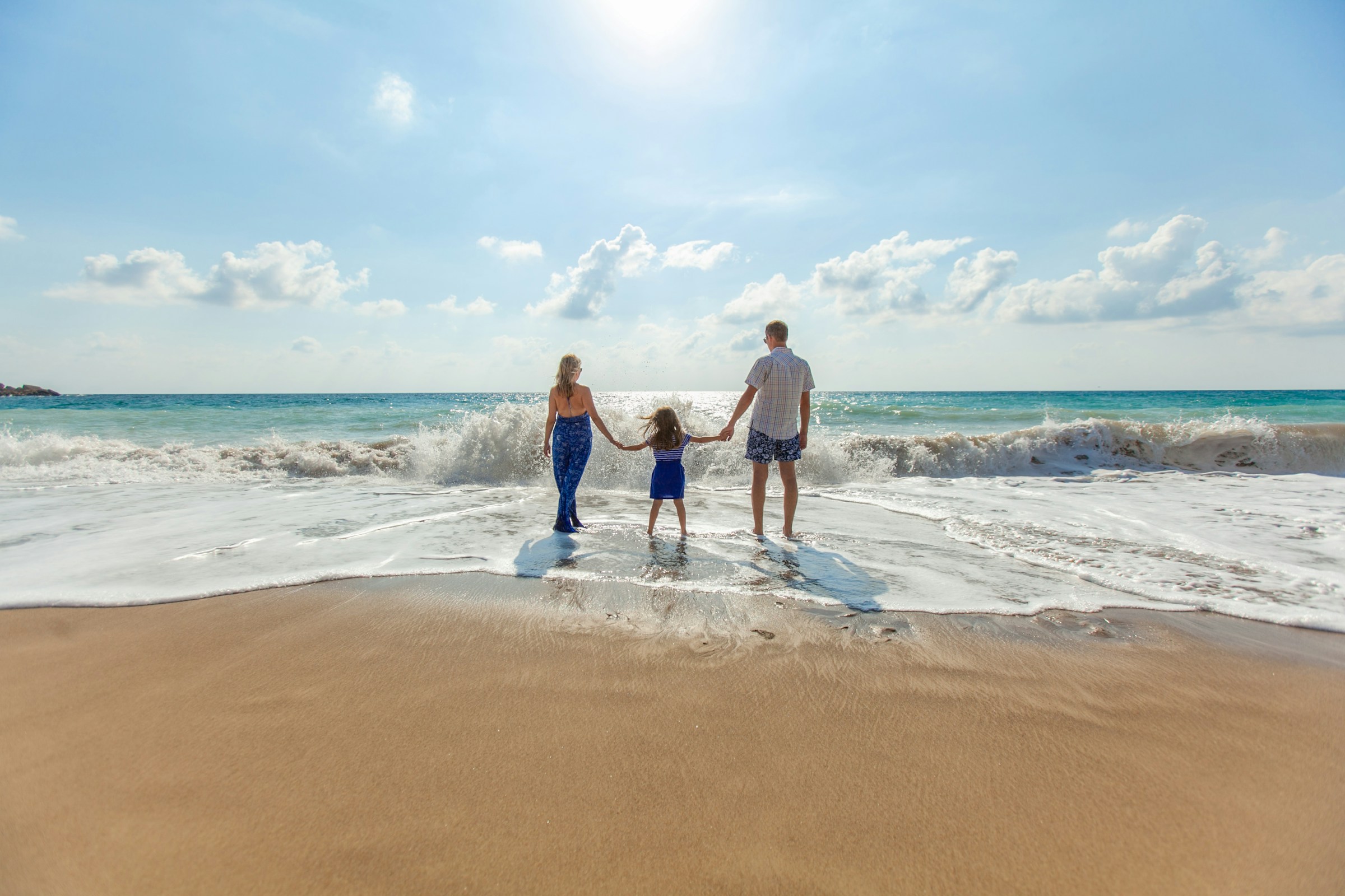 Two adults and a child holding hands together at the edge of the sea