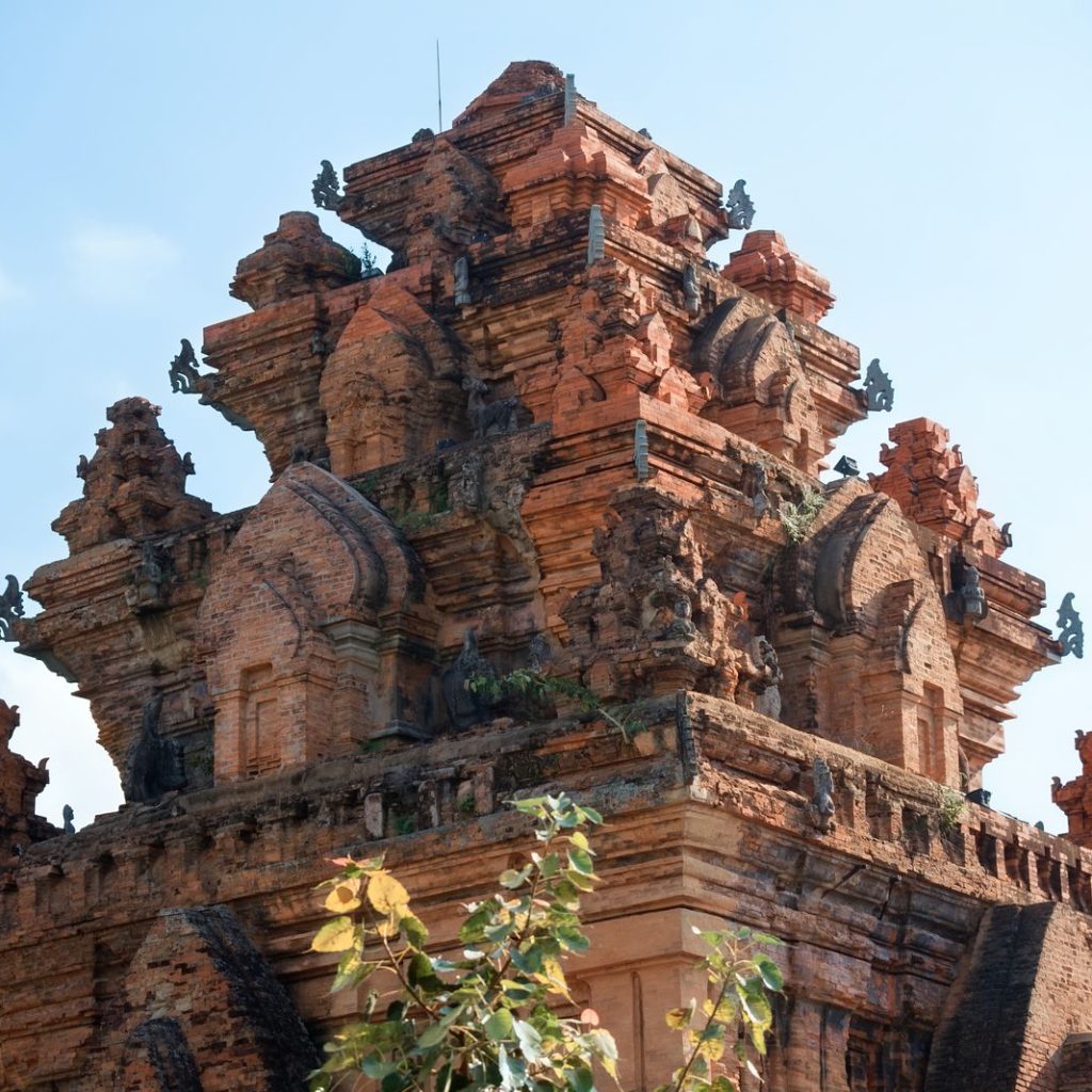 Weathered red-brick Cham tower with tiered carvings beneath a blue sky