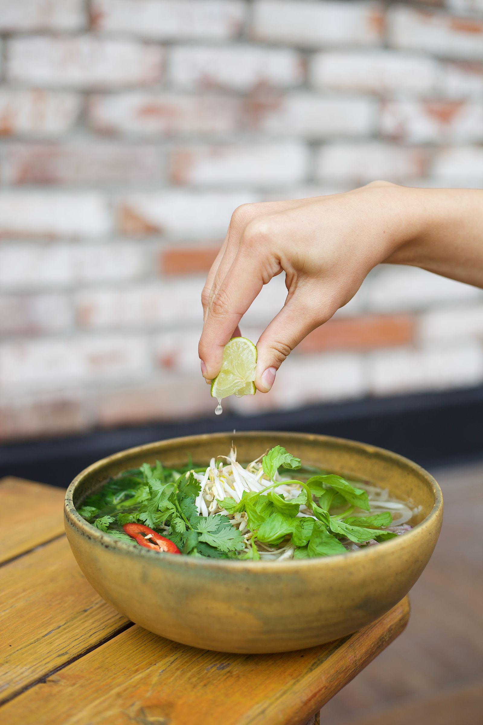 Bowl of chicken pho with clear broth, pale chicken slices, herbs and a squeeze of lime