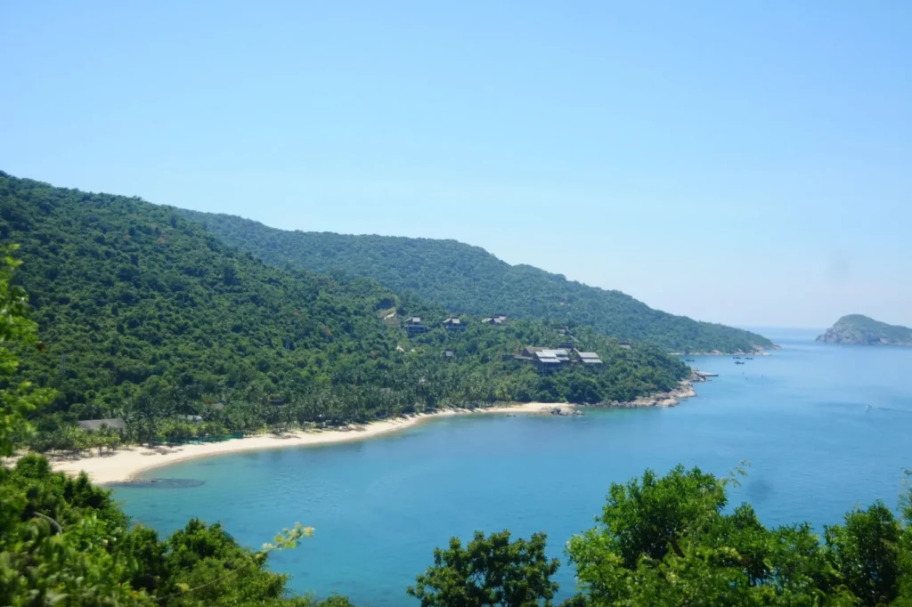 Forested hillside, sandy coastline and blue water at the Cham Islands